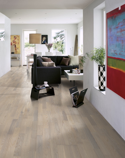 Ljust vardagsrum med parkettgolv, svart soffa, soffbord, konstverk på väggen och stora fönster som släpper in ljus.